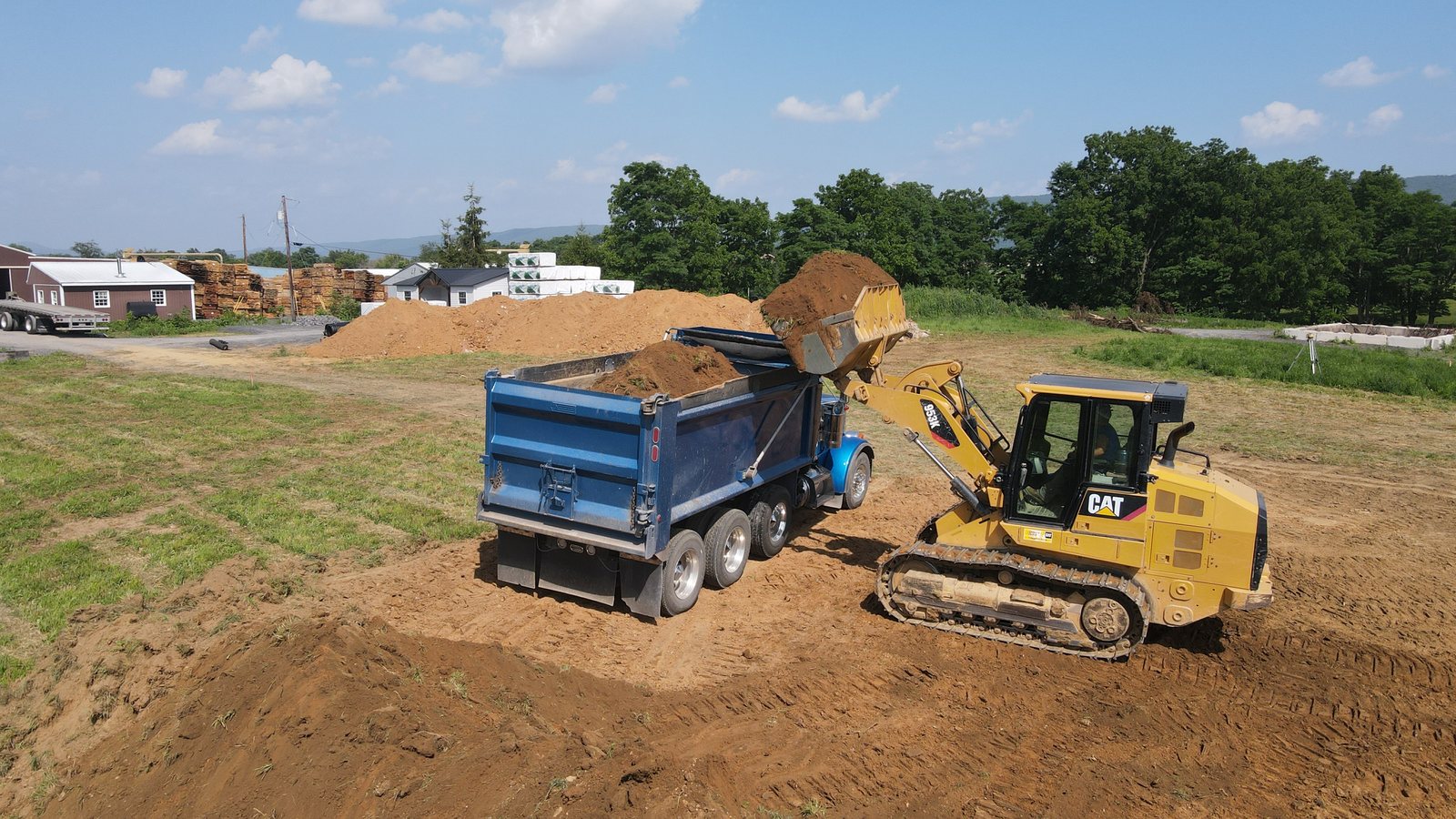 A log home building site being prepared, with excavation equipment grading the ground ahead of the foundation work