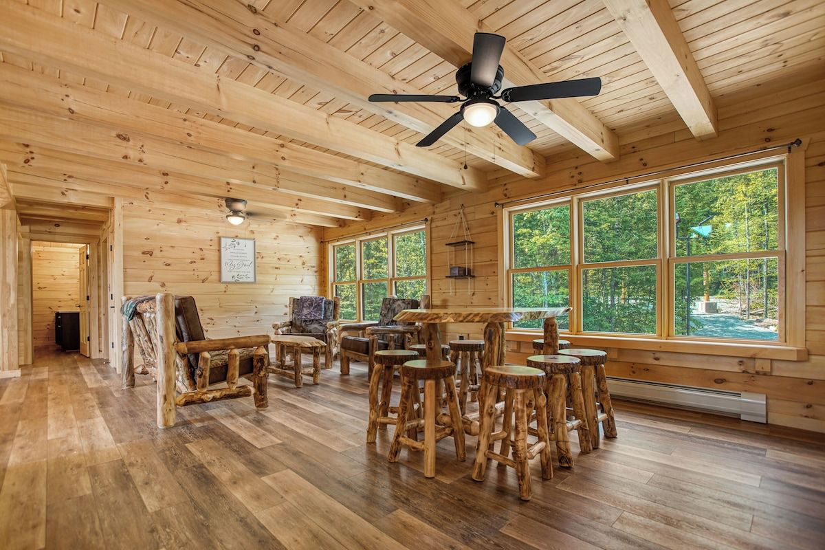A&A Cabin lounge with log furniture, high-top table and forest views