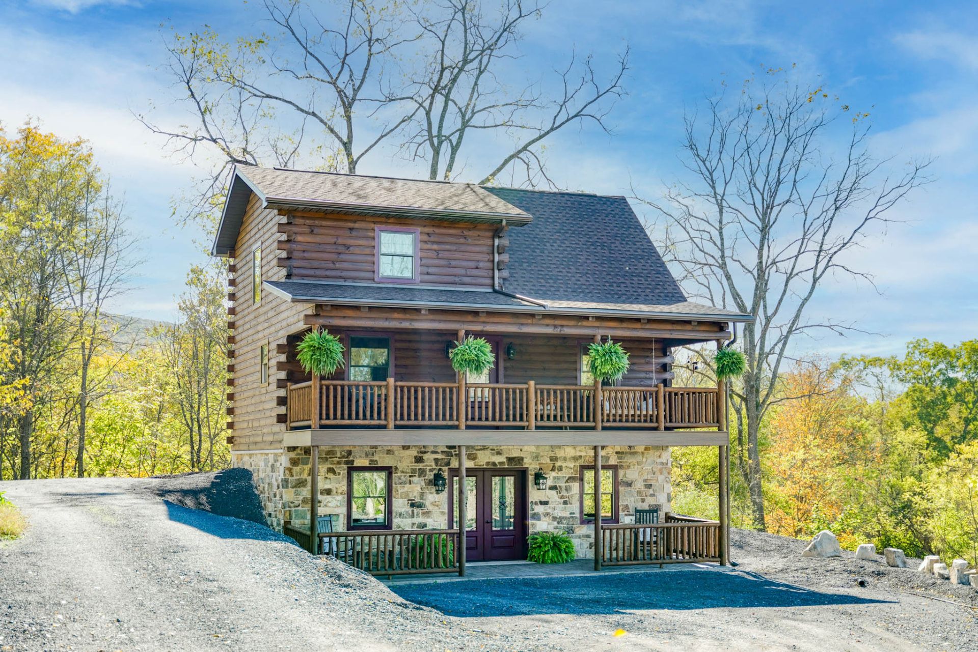 Two-story white pine log cabin with covered porches and stone foundation on a Pennsylvania hillside