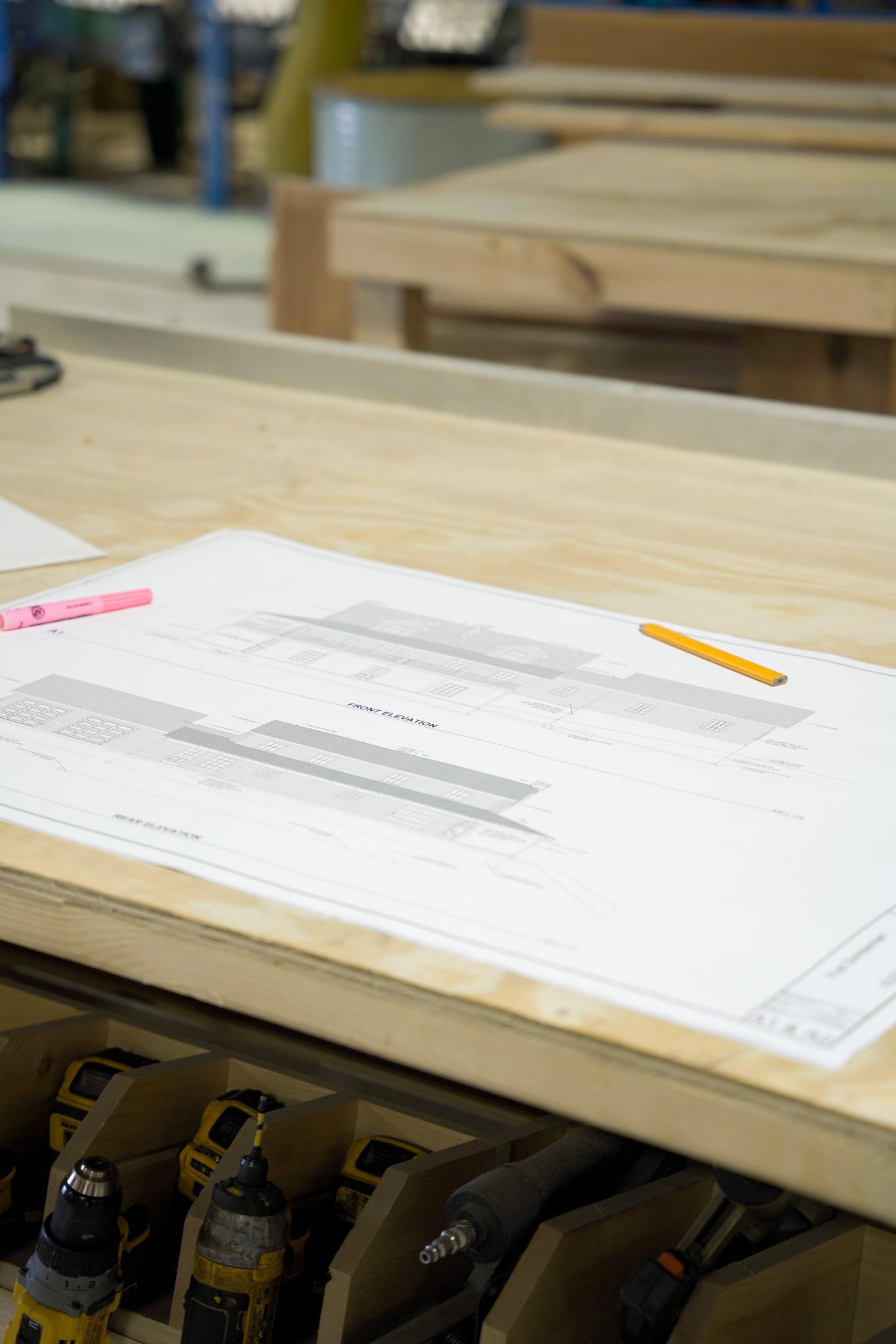 A KSM blueprint showing front and rear elevations laid out on a workbench in the Mifflintown shop with a pencil and highlighter